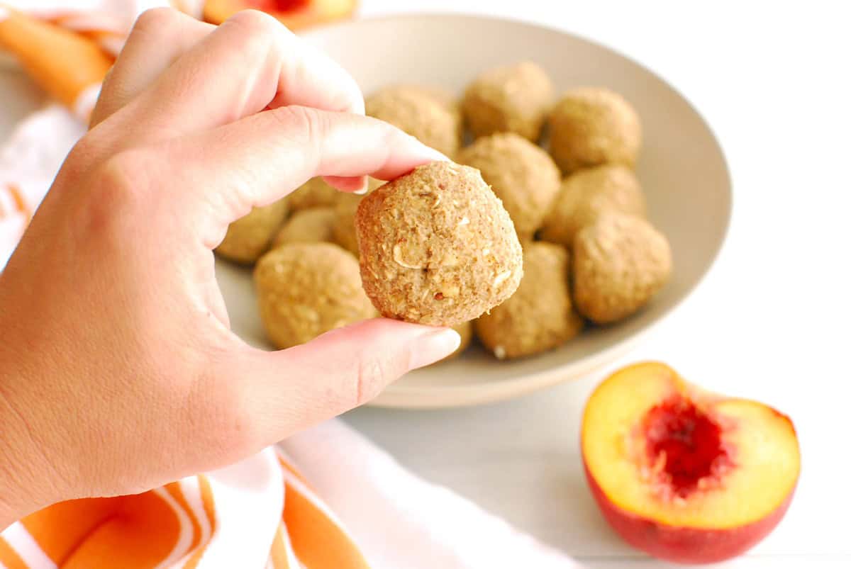A woman's hand holding a peach energy bite.